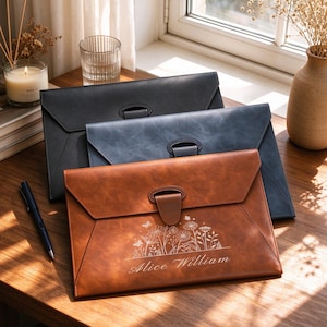 May include: Three rectangular document folders with envelope-style flaps and central tab closures. The front folder is brown with a white floral engraving and the name Alice William. The others are solid black and blue leather-like material.