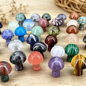 May include: A collection of small, mushroom-shaped figurines in various colors and patterns. The figurines are made of different types of stone, including tiger's eye, amethyst, and malachite. The mushrooms are arranged on a light-colored wooden surface.