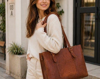 Op de afbeelding: Een bruine leren tote bag met een rechthoekige vorm, met een voorvak en verstelbare bandjes. De tas heeft een klassiek ontwerp met metalen hardware en wordt gedragen door de schouderbanden. De tas is gemaakt van rijk, getextureerd leer.