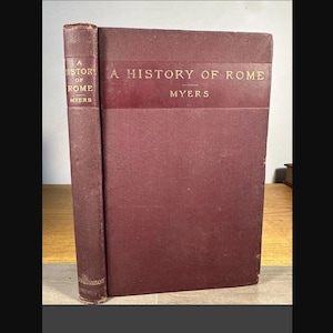 May include: A hardcover book titled A History of Rome by Myers with a deep maroon textured cover. The front cover and the spine feature the title and author name printed in gold lettering. The book has a rectangular shape and a vertical spine.