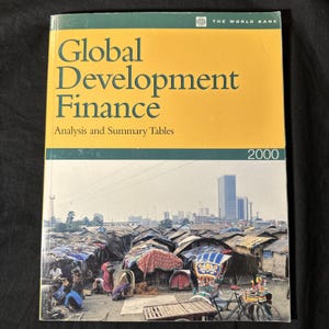 May include: A softcover book titled Global Development Finance Analysis and Summary Tables 2000 by The World Bank. The cover features a yellow top section with dark green text and a bottom photograph of a city skyline above a shantytown.