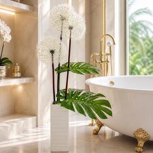 May include: A decorative floral arrangement featuring three large, white, spherical flower heads with dark stems and green leaves in a white, rectangular vase. The arrangement is in a luxurious bathroom setting with a white bathtub and gold fixtures.