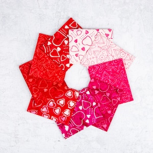 May include: A circular arrangement of fabric squares in shades of red and pink, patterned with hearts and other designs. The squares are arranged around a white center, creating a visually appealing, Valentine's Day themed display.