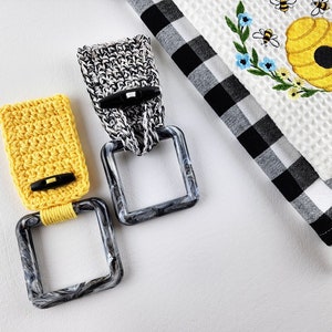 May include: Two crocheted towel rings with black and white marbled plastic rings. One ring is yellow and the other is black and white.