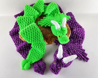 May include: Two crocheted dragon toys. One is green with white horns and the other is purple with white horns. Both are lying on a wooden surface.