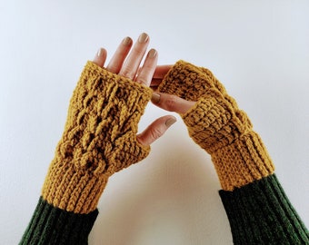 May include: A pair of mustard yellow fingerless gloves with a cable knit pattern. The gloves are worn on a person's hands with the cuffs folded down.