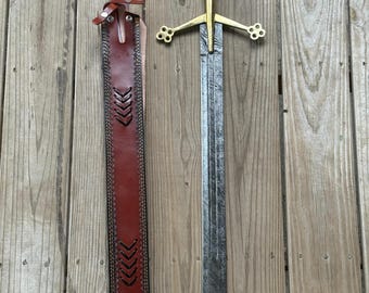 May include: A sword with a patterned Damascus steel blade, a polished brass crossguard featuring four-lobed ends, and a dark brown wooden grip with a brass pommel. Beside it lies a matching reddish-brown leather scabbard with decorative stitching.