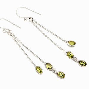 Könnte beinhalten: Silberne Hängeohrringe mit drei ovalen, hellgrünen Peridot-Edelsteinen. Die Ohrringe haben ein Ketten-Design und sind vor einem weißen Hintergrund platziert. Die Ohrringe sind etwa 7.6 cm lang.