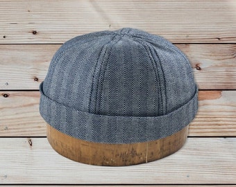 May include: A gray and white herringbone patterned beanie hat on a wooden display stand.