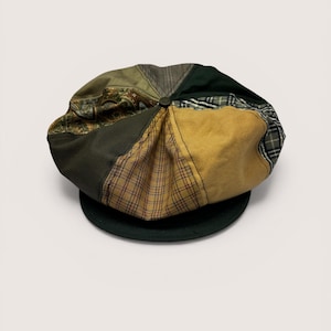 Peut inclure: Casquette de style gavroche en patchwork avec des tissus verts, marron et beige. La casquette a un bord vert foncé et un bouton au centre. Les tissus comprennent des motifs à carreaux, unis et à motifs.