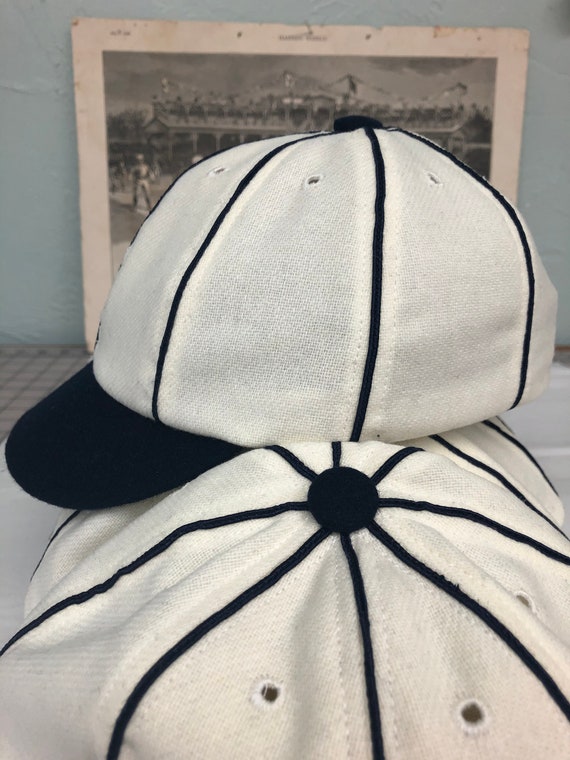 Detroit Vintage Base Ball 1859 Team cap. White wool flannel 8 panel with large black button, soutache, and short soft visor.