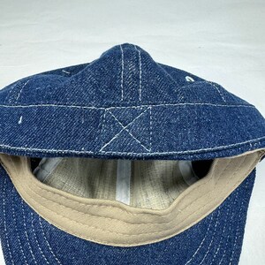 K&ouml;nnte beinhalten: Blaue Jeans-Cap mit wei&szlig;en N&auml;hten. Die Cap hat einen gebogenen Schirm und ein beigefarbenes Innenfutter. Die N&auml;hte bilden ein Kreuzmuster auf der Oberseite.