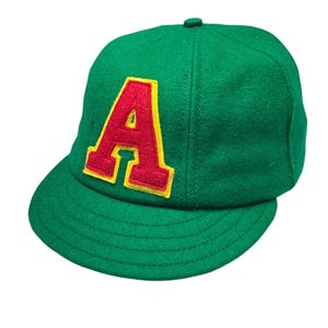 May include: A green baseball cap with a large red felt letter "A" on the front. The letter has a yellow outline.