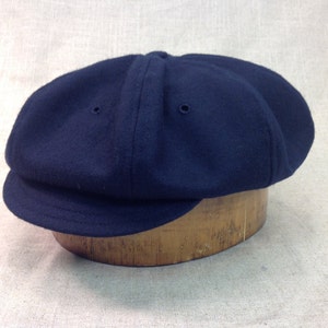 May include: A navy blue wool newsboy cap with a rounded crown and a short brim.