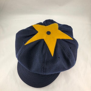 May include: A navy blue wool cap with a yellow star on the top. The cap has a brim and a button on the top.