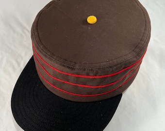 Brown cotton twill boxcap with Black 2.5” visor, yellow button, red soutache trim, fitted to any size.