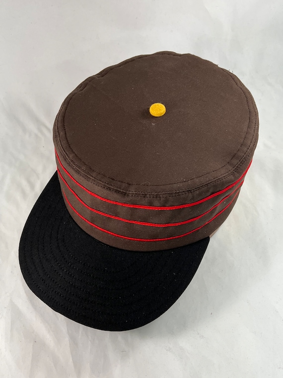 Brown cotton twill boxcap with Black 2.5” visor, yellow button, red soutache trim, fitted to any size.