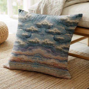May include: A square throw pillow featuring a textured, layered pattern of clouds in shades of blue, white, and soft pink. The design consists of intricate, wavy, stitched lines that create a three-dimensional effect across the surface.