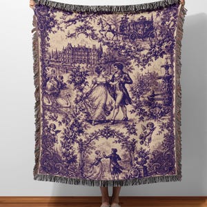 May include: A purple and cream throw blanket with a romantic toile pattern. The design shows couples dancing, cherubs, swans, and horse-drawn carriages. The edges are finished with a fringe.