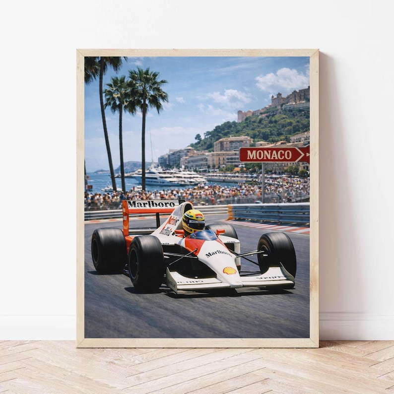 May include: Framed print of a Formula 1 race car speeding on a track in Monaco. The car is white with red and orange accents and the Marlboro logo. Palm trees, a harbor, and a sign that says "Monaco" are in the background.