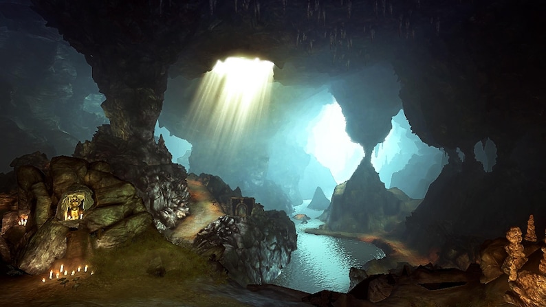 May include: A dark cavern interior featuring a natural rock opening that allows bright sunlight to stream down in rays. A small, glowing golden statue sits within a recessed rock niche, illuminated by a cluster of small white candles on the ground.