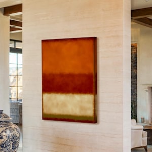 Può includere: Un dipinto astratto con fasce orizzontali di colore. La fascia superiore è arancione caldo, seguita da un rosso intenso e un beige chiaro in basso. L'opera d'arte è esposta su una parete strutturata in una stanza ben illuminata.