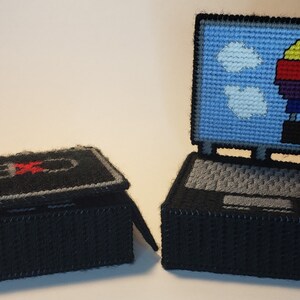 May include: Two black and gray crocheted laptop boxes. One box is open and the other is closed. The open box has a blue screen with a hot air balloon and clouds. The closed box has a black screen with a red power button.