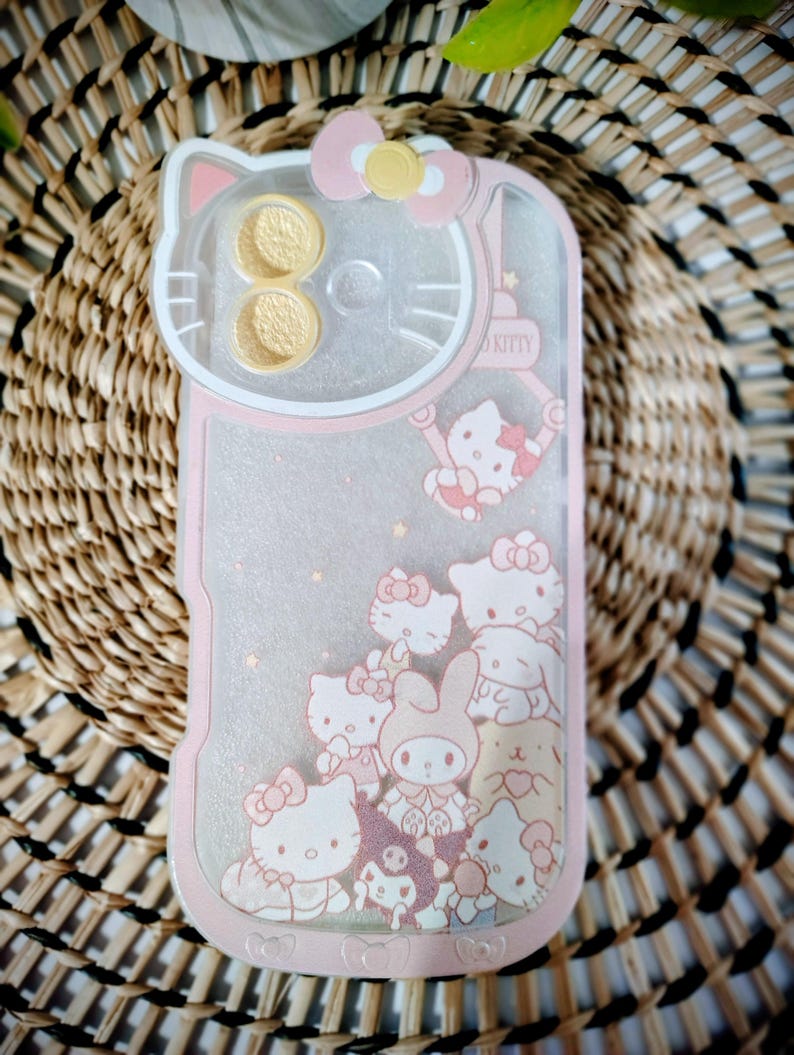 May include: Pink and clear phone case featuring a Hello Kitty design. The case has a pink border and a clear center with glitter and Hello Kitty characters. The top of the case has a Hello Kitty head design with a pink bow.