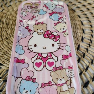 May include: Pink phone case featuring Hello Kitty and teddy bear illustrations. The case has a vertical striped background with hearts, bows, and clouds. The design includes blue, pink, and brown teddy bears and Hello Kitty.