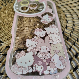 May include: Pink phone case featuring a clear design with multiple cartoon characters. The case has a pink border and a clear back with images of Hello Kitty and other characters. The case is designed to fit a phone.