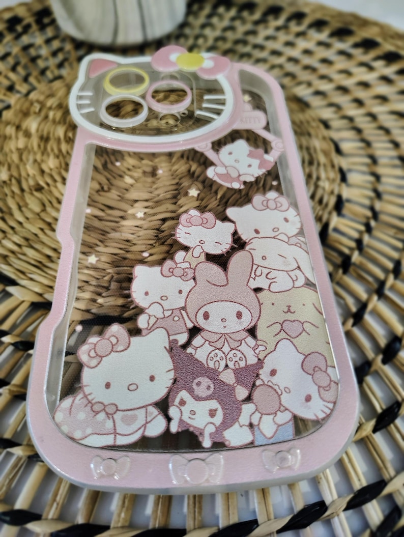 May include: Pink phone case featuring a clear design with multiple cartoon characters. The case has a pink border and a clear back with images of Hello Kitty and other characters. The case is designed to fit a phone.