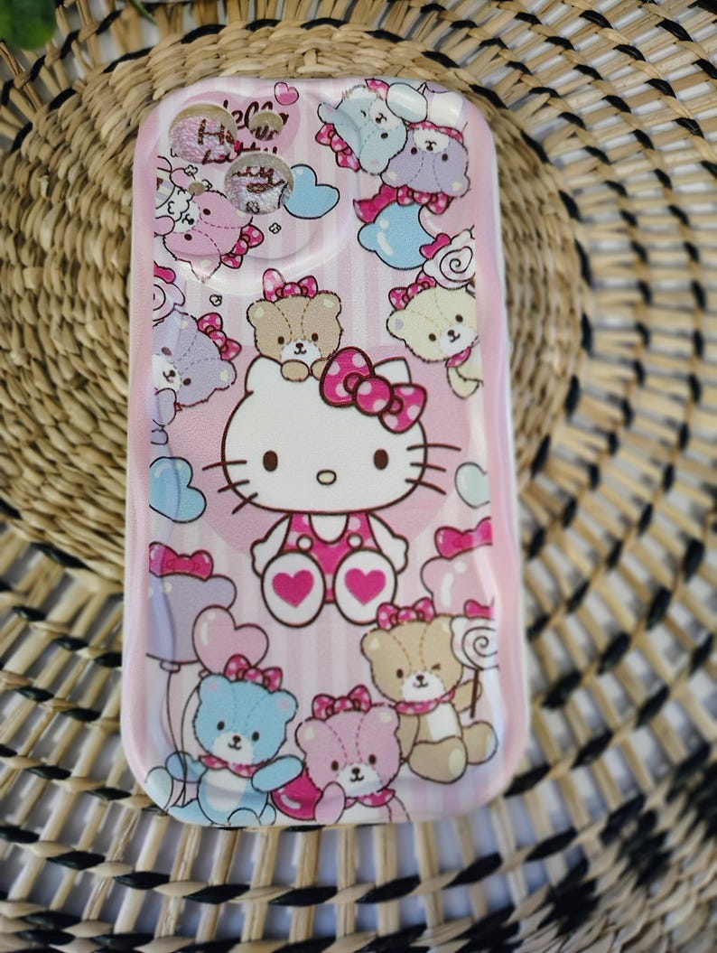 May include: Pink phone case featuring Hello Kitty and teddy bear graphics. The case has a glossy finish and is decorated with bows, hearts, and clouds. The design includes light blue, pink, and brown colors.