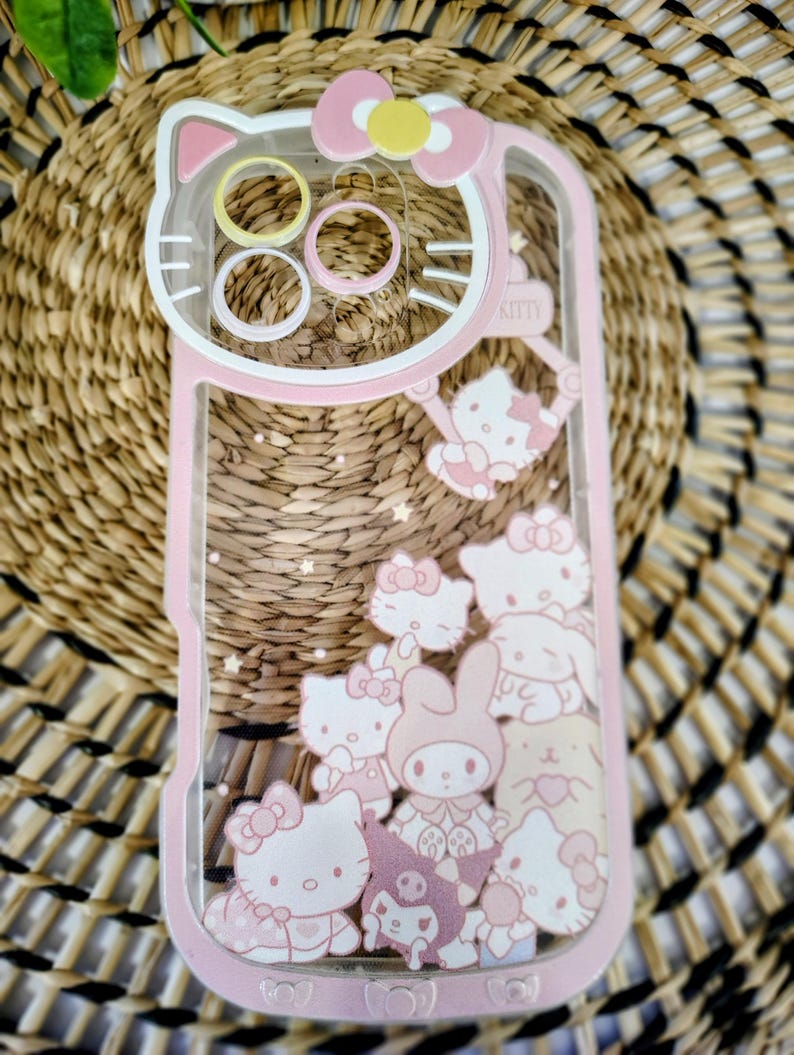 May include: Pink and clear phone case featuring a Hello Kitty design. The case has a pink border and a clear center filled with Hello Kitty characters and stars. The top of the case has a Hello Kitty head shape.