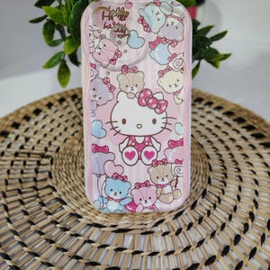 May include: Pink phone case featuring Hello Kitty and teddy bear graphics. The case has a vertical striped pattern and the words "Hello Kitty" are visible. The case is decorated with hearts and bows.