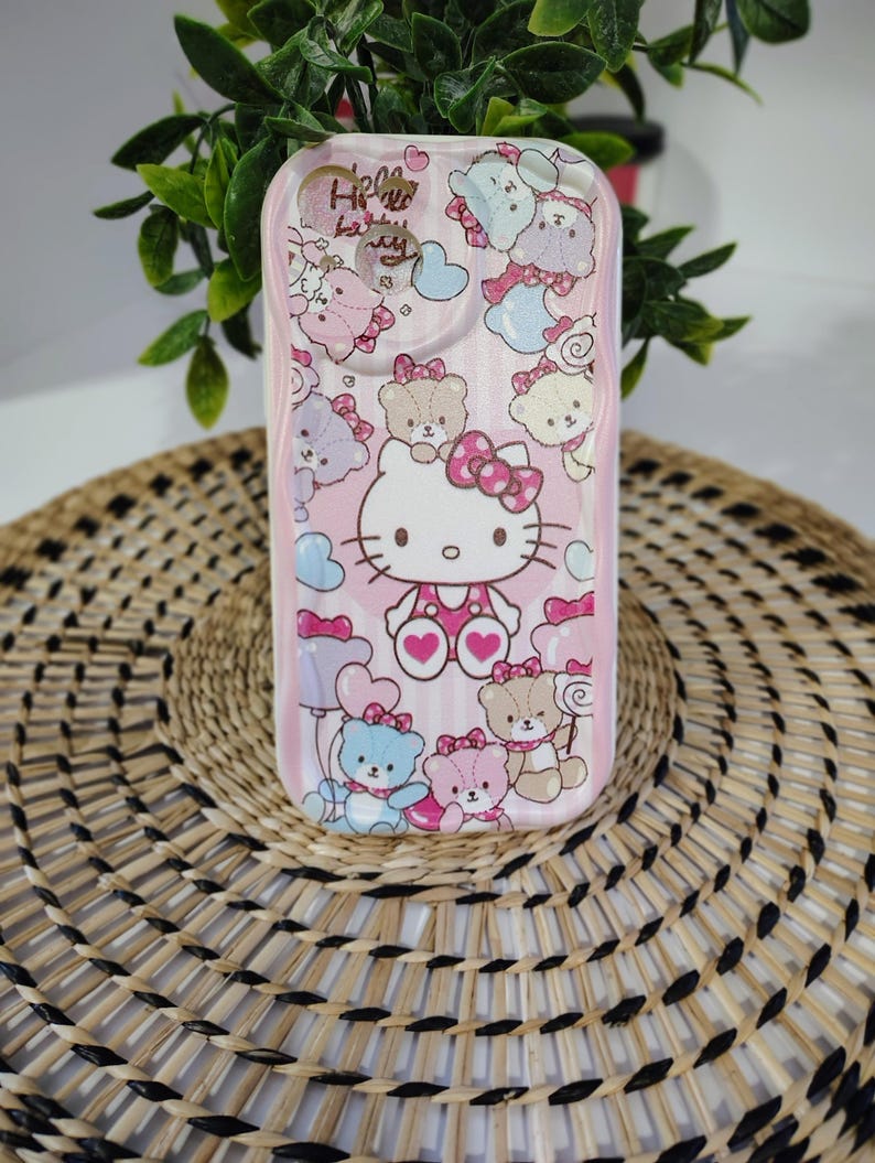 May include: Pink phone case featuring Hello Kitty and teddy bear graphics. The case has a vertical striped pattern and the words "Hello Kitty" are visible. The case is decorated with hearts and bows.