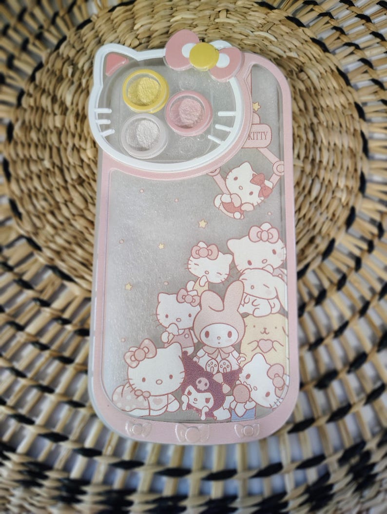 K&ouml;nnte beinhalten: Rosa-wei&szlig;es Handyh&uuml;lle mit Hello Kitty und anderen Zeichentrickfiguren. Die H&uuml;lle hat eine transparente R&uuml;ckseite, einen rosa Rand und ein Hello Kitty-Gesichtsmotiv oben. Der Text "KITTY" ist auf der Seite sichtbar.
