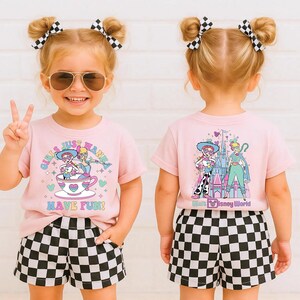 May include: A child in a light pink t-shirt and black and white chequered shorts. The front of the tee has the text "GIRLS JUST WANNA HAVE FUN!" with a cartoon graphic. The back of the shirt has a Disney graphic.