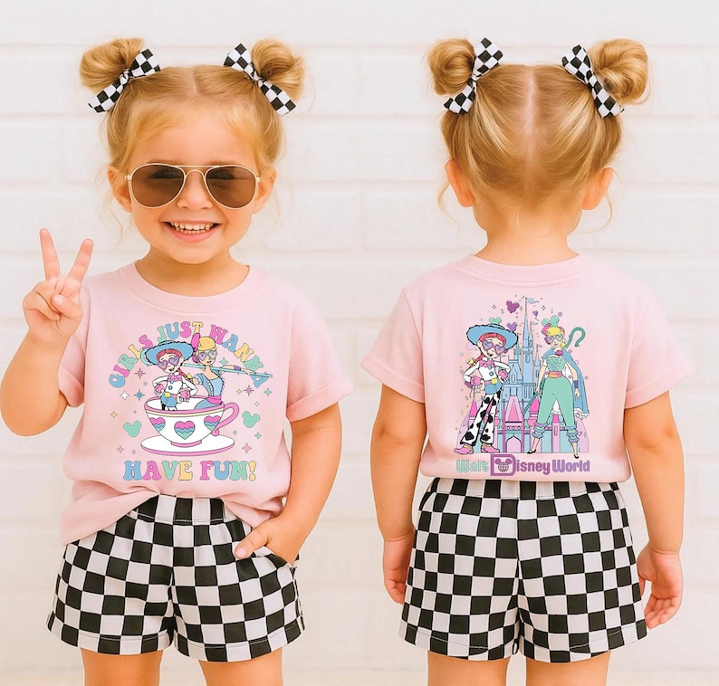May include: A child in a light pink t-shirt and black and white chequered shorts. The front of the tee has the text "GIRLS JUST WANNA HAVE FUN!" with a cartoon graphic. The back of the shirt has a Disney graphic.