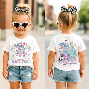 May include: A white t-shirt with a colourful graphic featuring cartoon characters and the text "GIRLS JUST WANNA HAVE FUN!". The shirt is paired with denim shorts. The back of the shirt has a "Walt Disney World" graphic.