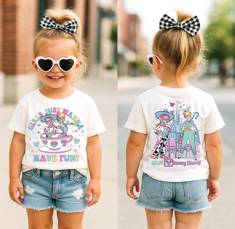 May include: A white t-shirt with a colourful graphic featuring cartoon characters and the text "GIRLS JUST WANNA HAVE FUN!". The shirt is paired with denim shorts. The back of the shirt has a "Walt Disney World" graphic.