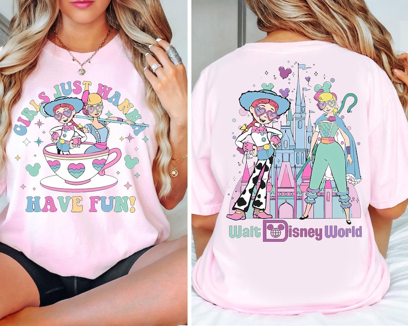 May include: Pale pink t-shirt with a vibrant graphic. The front displays two cartoon characters in a teacup, with the text "GIRLS JUST WANNA HAVE FUN!". The back features two characters in front of a castle, with the text "Walt Disney World".