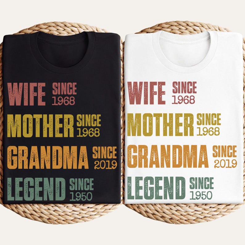 Pu&ograve; includere: Due magliette, una nera e una bianca, con le parole "WIFE SINCE 1968, MOTHER SINCE 1968, GRANDMA SINCE 2019, LEGEND SINCE 1950" stampate in vari colori. Le magliette sono esposte su un cestino intrecciato.