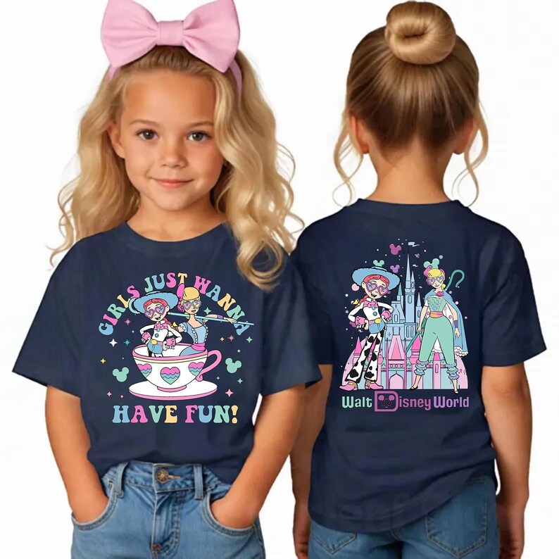 May include: Navy blue t-shirts with vibrant graphics. One shirt displays the text "GIRLS JUST WANNA HAVE FUN!" and a cartoon of two characters in a teacup. The other shirt has a graphic of two characters and a castle with the text "Walt Disney World".