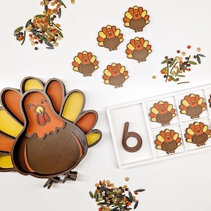 May include: A large turkey-shaped tray with brown, orange, and yellow sections, accompanied by a white rectangular tray containing six small turkey-shaped pieces and a brown number six, surrounded by scattered autumn-themed sprinkles.