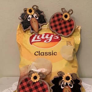 May include: Three fall-themed bag toppers, two are red and black plaid pumpkins with yellow sunflowers and brown burlap bows, and one is a black crow with a yellow sunflower and brown burlap bow. The toppers are on a bag of Lay's Classic potato chips.