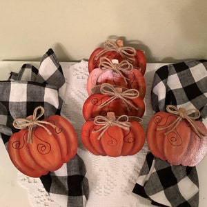 May include: Set of eight hand-painted wooden pumpkin napkin rings in shades of orange and pink with black and white checkered napkins. The pumpkins have a rustic, farmhouse style.