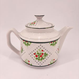May include: White ceramic teapot with a lid, handle, and spout. The teapot features a strawberry pattern with red berries and green leaves on a light gray background. The lid and rim have a green border.