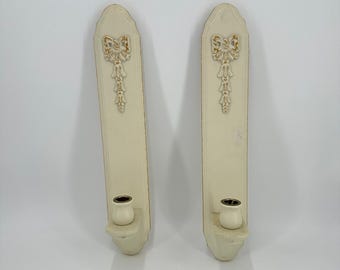 Juego de 2 portavelas de pared vintage color blanco roto con lazo dorado y borla, de madera ornamentada.