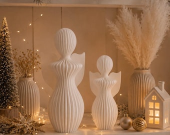 Op de afbeelding: Twee witte, verticaal geribbelde engelfiguren met gladde, ronde hoofden en gestileerde vleugels. De grotere engel staat links van de kleinere, beide hebben een consistente, gegroefde textuur over hun langwerpige, symmetrische lichamen.