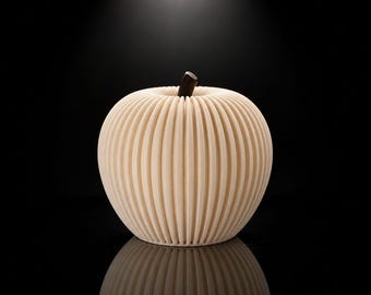 Op de afbeelding: Een crèmekleurig, bolvormig decoratief object in de vorm van een appel, voorzien van een reeks verticale, accordeonachtige plooien of ribbels die vanuit het midden uitstralen. Een kleine, donkerbruine, cilindrische steel bevindt zich in het midden.